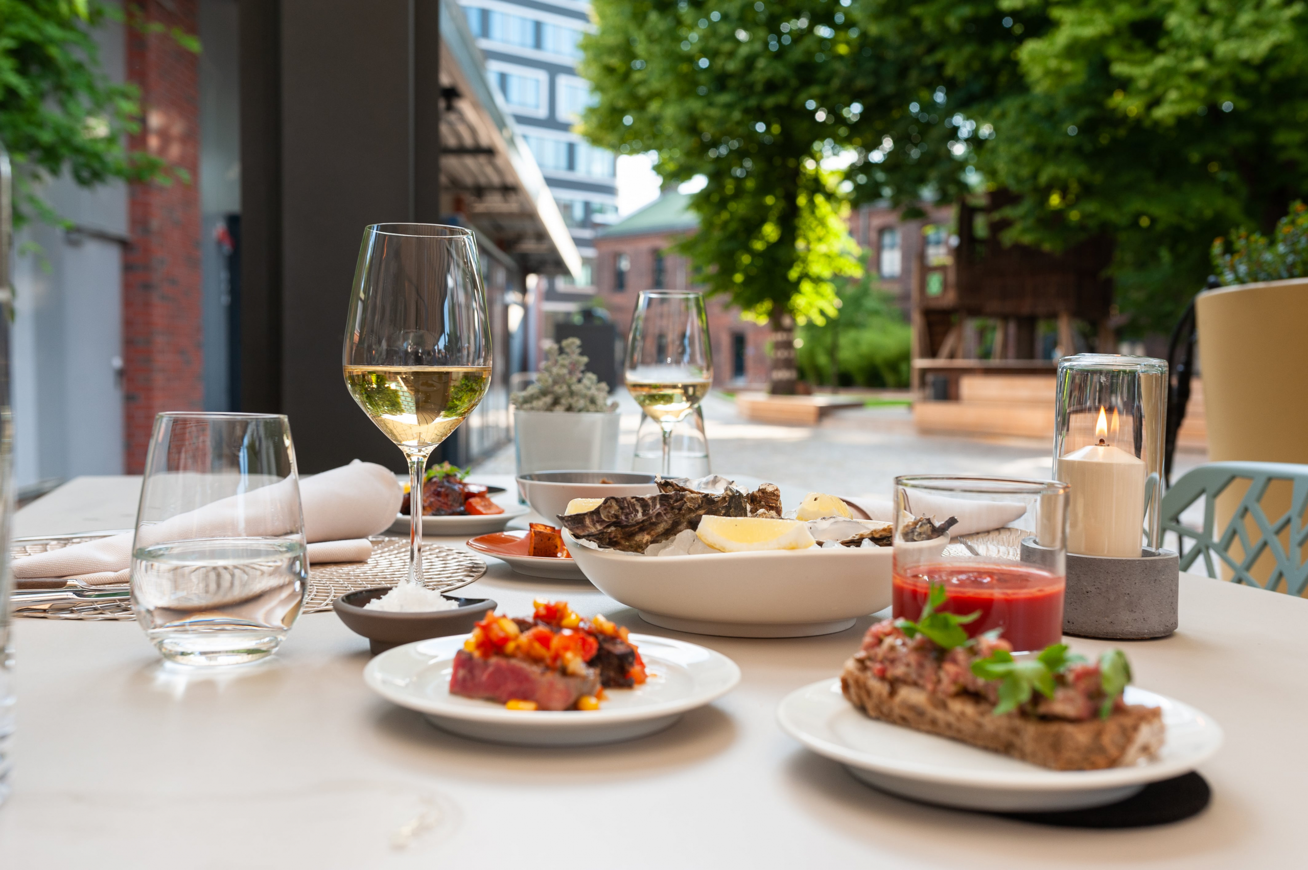 Ein gedeckter Tisch mit kleinen Tellern und Speisen, die Sonne scheint, die Weingläser sind gefüllt